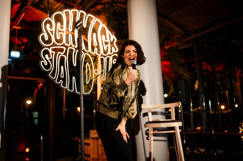 Comedienne mit Mikrofon vor dem SCHNACK Stand-Up Neonschild